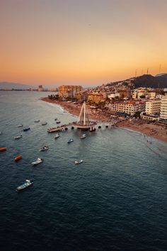 boats are on the water in front of a city and beach at sunset or dawn