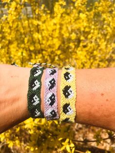 a person's arm with four bracelets on it and yellow flowers in the background