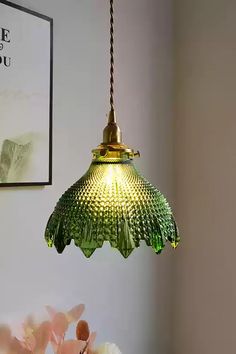 a green glass light hanging from a ceiling in a room with flowers on the table