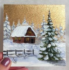 a hand holding up a small card with a painting of a cabin in the snow