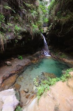 there is a small pool in the middle of some rocks and water with a waterfall coming out of it