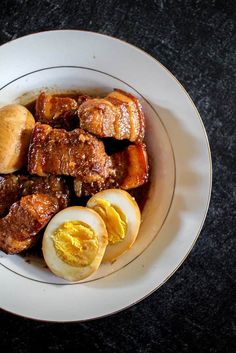 a white bowl filled with meat and eggs on top of a black countertop next to an orange peel