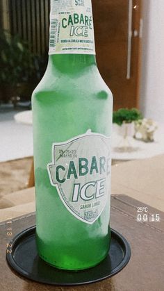 a bottle of cabar ice sitting on top of a wooden table next to a plant