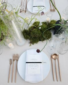 the table is set with white plates, silverware and moss covered napkins on it