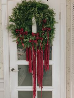 a wreath hanging on the front door of a house with red ribbons and greenery