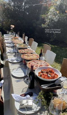 a long table is set up with pizzas and wine for an outdoor dinner party