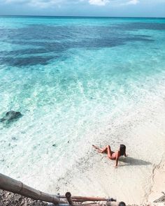 a woman laying on top of a sandy beach next to the ocean with clear blue water