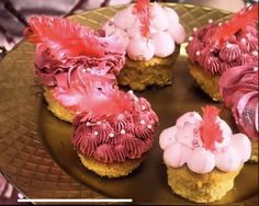 four cupcakes decorated with pink and red icing on a gold platter