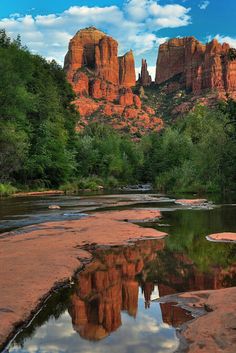 the red rock formations are reflected in the still water of the river, with trees and bushes around them