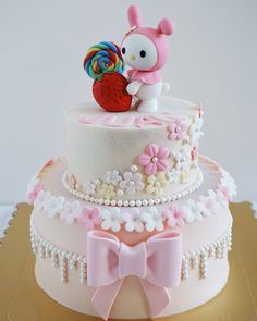 a hello kitty cake is decorated with pink and white flowers, candy, and a strawberry