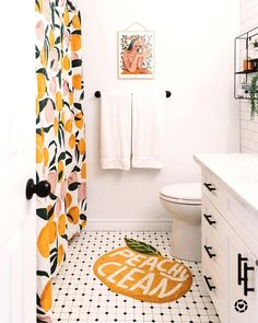 a white bathroom with orange and green decor on the shower curtain, toilet seat cover, and rug