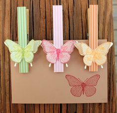 three butterflies are hanging on a piece of brown paper with pink, yellow and green ribbons