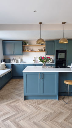 a kitchen with blue cabinets and white counter tops, wooden flooring and gold pendant lights