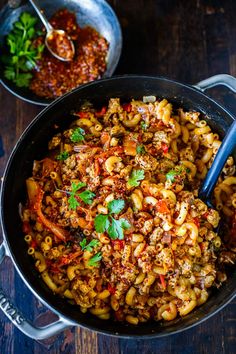 a skillet filled with pasta and meat on top of a wooden table next to other dishes