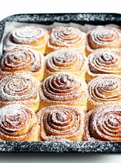 a pan filled with cinnamon rolls covered in powdered sugar on top of a table