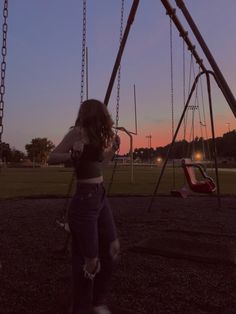 a woman standing on top of a swing set at dusk with the sun setting in the background