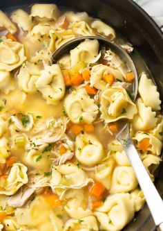 a pot filled with chicken noodle soup on top of a white table cloth next to a silver spoon