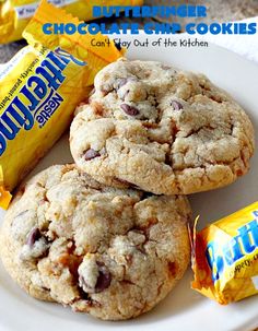 three chocolate chip cookies on a white plate next to candy bar wrappers and a bag of butterfingers