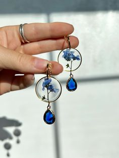 a person is holding some kind of earrings with blue flowers on the dangles