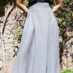 a woman standing in front of a stone wall wearing a black top and blue skirt