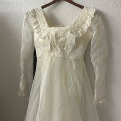 a white dress hanging on a hanger in front of a wall with a coat rack