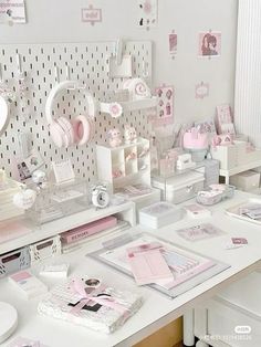 a white desk topped with lots of pink and white items next to a wall covered in pictures