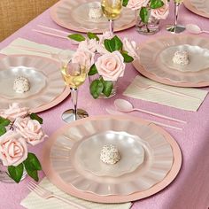 the table is set with pink and white plates, silverware, and flowers in vases