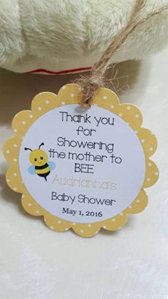 a white teddy bear sitting next to a yellow and white tag that says thank you for showering the mother to bee