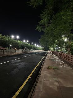 an empty street at night with lights on and trees lining the side walk in the foreground