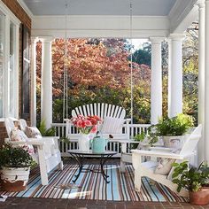 a porch with chairs, tables and potted plants on the front porch area that is painted white