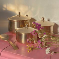 three pots and two spoons sitting on top of a pink table with purple flowers