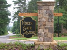 the sign for north gate manor is in front of some bushes and trees on either side of the road