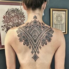 the back of a woman's neck with an intricate tattoo design on her lower back