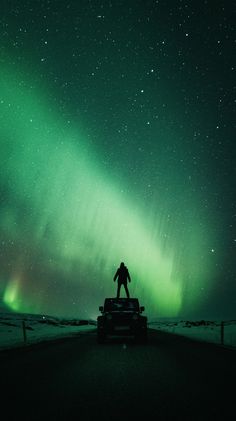 a man standing on the back of a truck under an aurora bore