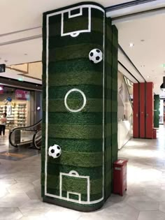 a large green sign in the middle of a mall with soccer balls and goal on it