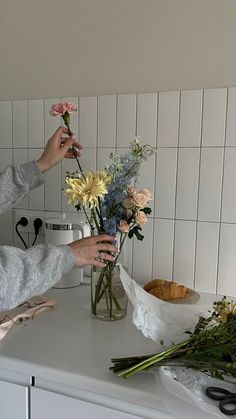 a woman arranging flowers in a vase on a counter