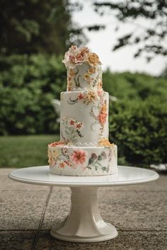 a three tiered wedding cake with flowers on the top is sitting on a white pedestal