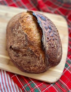 a loaf of bread sitting on top of a wooden cutting board next to a red and green checkered table cloth