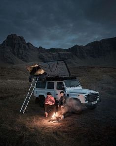 two people standing in front of a camper van with the roof open and lights on