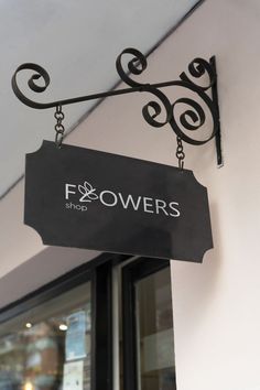 a sign hanging from the side of a building that says flowers shop on it's front