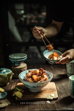 two people eating food from bowls with chopsticks in their hands on a wooden table