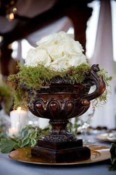 a vase with white flowers and greenery on top of a table at a wedding