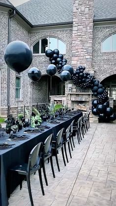 a long table is set up with black balloons and place settings for an outdoor party