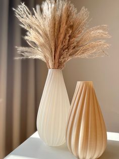 two vases with dried grass in them on a table