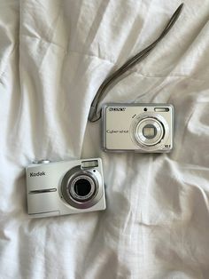 two cameras sitting on top of a bed next to an unmade white comforter