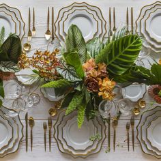 the table is set with plates, silverware and floral centerpieces on it