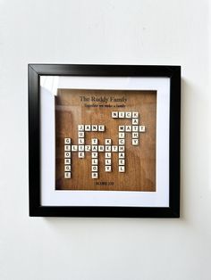 a wooden crossword puzzle in a black frame on a white wall with the words the buddy family written across it