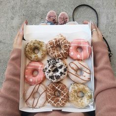 a person holding a box of donuts with sprinkles