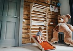 a little boy sitting in front of a large teddy bear next to a wooden ladder