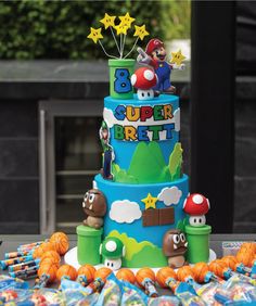 a blue and green birthday cake with mario bros characters on the top, surrounded by candy candies